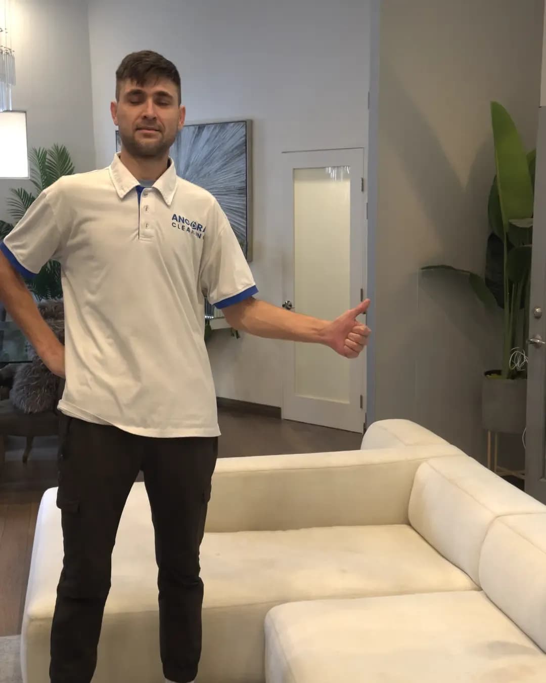 Man in a polo shirt gesturing beside a white modern sofa in a living room.